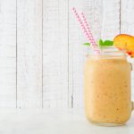 Peach smoothie in a mason jar glass with paper straws.  Side view with a white wood background.
